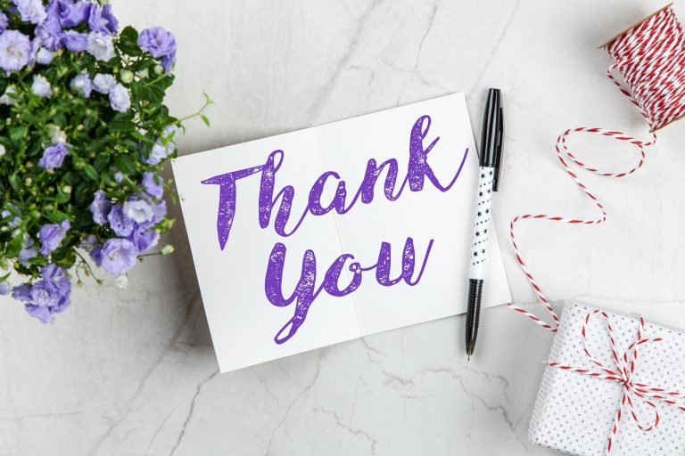 Papel com escrito "Thank You" em cima de uma superfície, com flores e caneta ao lado. Indica gratidão. Créditos: Pexels.